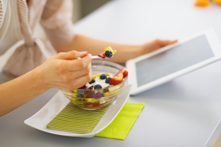 Closeup on young woman eating fruits salad and using tablet pcの写真素材