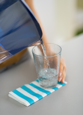 Closeup on housewife pouring water into glass from water filter pitcherの写真素材