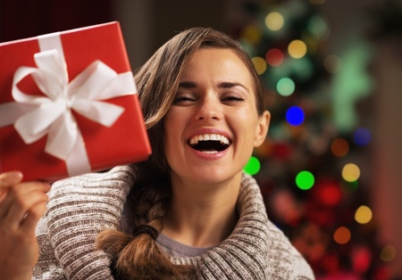 Happy young woman looking out from present box in front of christmas lightsの写真素材