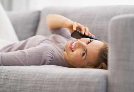 Smiling young woman talking mobile phone while laying on couchの写真素材