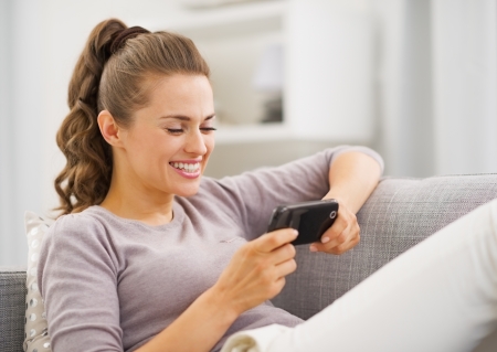 Happy young woman reading sms while sitting on couchの写真素材