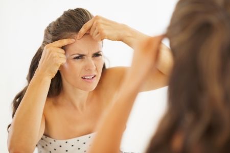 Concerned young woman squeezing acne in bathroomの写真素材