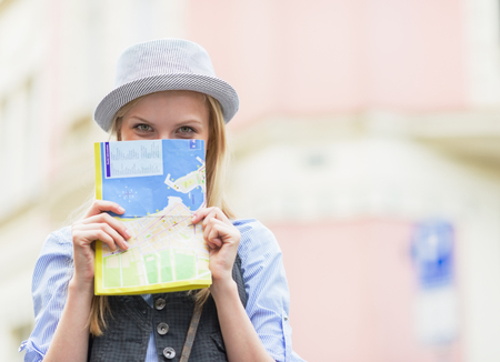 Tourist girl hiding behind map while standing on city streetの写真素材