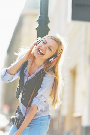 Happy hipster girl listening music on city street and dancingの写真素材