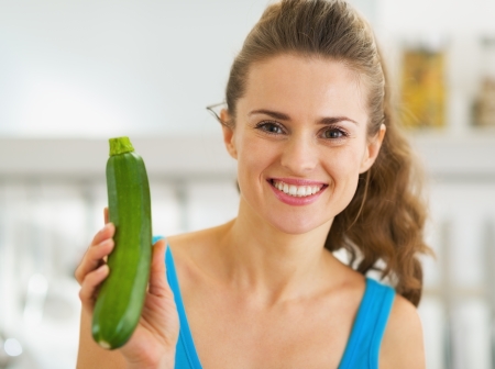 Smiling young woman showing fresh zucchiniの写真素材
