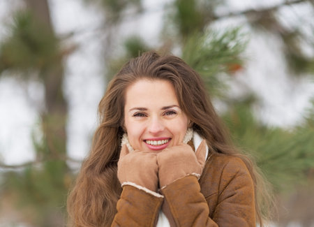 Portrait of happy young woman against fir-tree in winter outdoorsの写真素材
