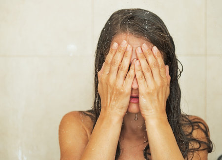 Stressed woman closing face with hands in showerの写真素材