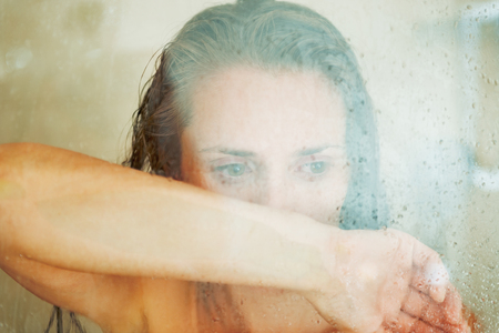 Stressed woman leaning on weeping glass shower doorの写真素材