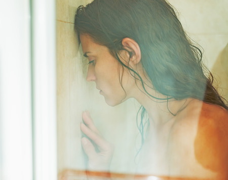 Frustrated woman leaning on weeping glass shower doorの写真素材