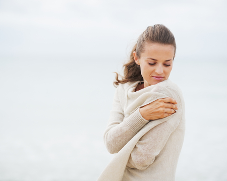 Young woman wrapping in sweater on coldly beachの写真素材