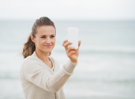 Happy young woman in sweater on beach taking photo using cell phoneの写真素材