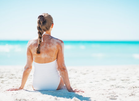 Young woman in swimsuit sitting on sandy beach . rear viewの写真素材