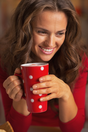 Happy young woman in christmas red dress having cup of hot beverageの写真素材