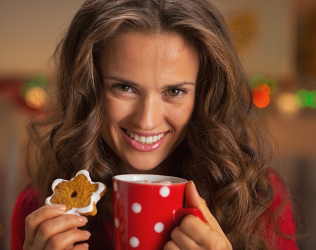 Portrait of smiling young woman with cup of hot chocolate and christmas cookieの写真素材