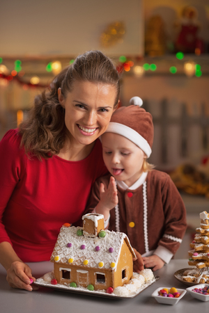 Portrait of smiling mother and baby with christmas cookie house in kitchenの写真素材