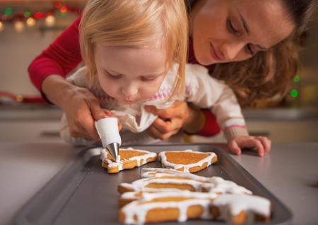Baby helping mother decorate homemade christmas cookies with glazeの写真素材