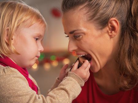 Baby giving mother bite of chocolate santaの写真素材