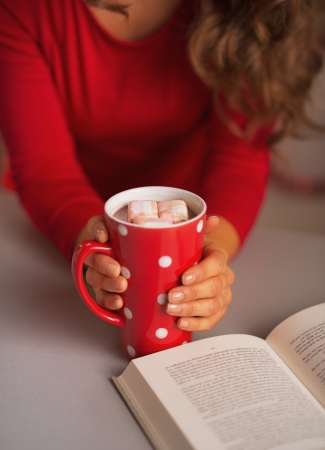 Closeup on book and cup of hot chocolate in hand of young womanの写真素材