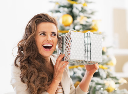 Excited young woman with christmas present box in front of christmas tree