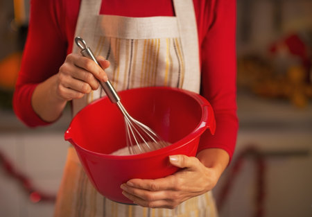 Closeup on young housewife using dough whisk