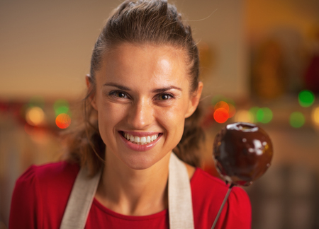 Portrait of smiling young housewife showing apple in chocolate glaze in kitchenの写真素材