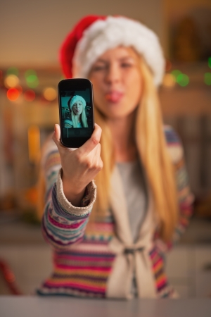 Closeup on cheerful teenage girl in santa hat taking self photo in christmas decorated kitchenの写真素材