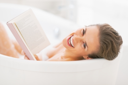Portrait of smiling young woman reading book in bathtub. rear viewの写真素材