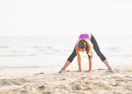 Healthy young woman stretching on beach