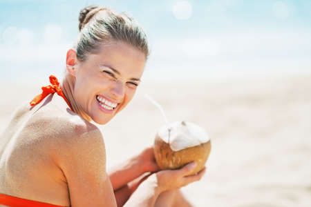 Smiling young woman sitting with coconut on beachの写真素材