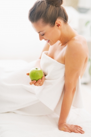Happy young woman with apple sitting on massage tableの写真素材