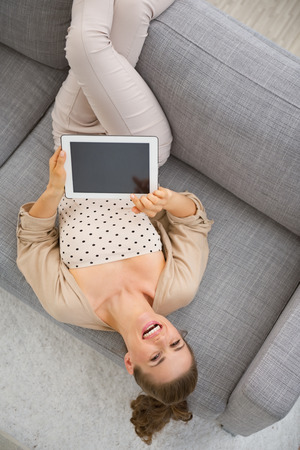 Smiling young woman laying on couch with tablet pcの写真素材