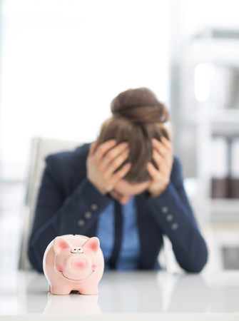 Closeup on piggy bank on table and stressed business woman in backgroundの写真素材