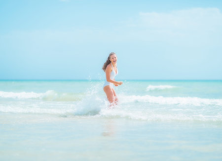 Happy young woman in swimsuit running into seaの写真素材