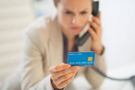 Closeup on business woman with credit card talking phone in officeの写真素材