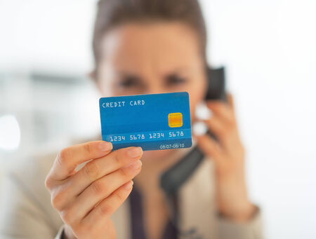 Closeup on business woman with credit card talking phone in officeの写真素材