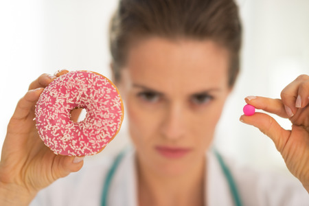 Closeup on serious medical doctor woman showing donut and pillの写真素材