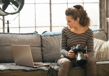 Young woman with modern dslr photo camera using laptop in loft apartment