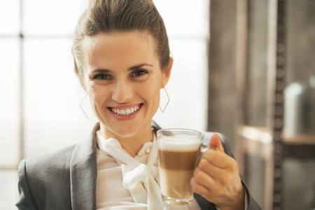 Portrait of smiling business woman drinking coffee latte in loft apartmentの写真素材