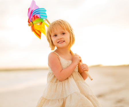 Portrait of baby girl holding colorful windmill toy on the beach in the eveningの写真素材