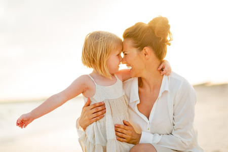 Portrait of happy mother and baby girl hugging on the beach in the eveningの写真素材
