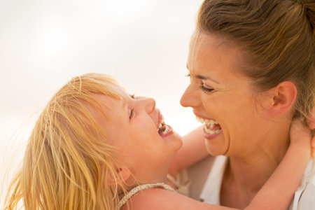 Portrait of smiling mother and baby girl hugging on the beach in the eveningの写真素材