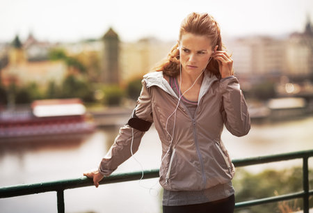 Fitness young woman in earphones in city in the evening