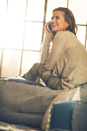 Happy young woman talking cell phone in loft apartmentの写真素材