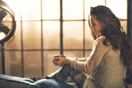 Young woman enjoying cup of coffee in loft apartmentの写真素材