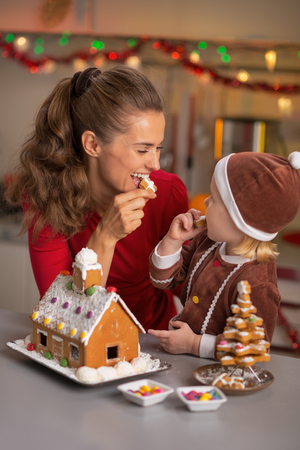 Happy mother and baby eating cookie in christmas decorated kitchenの写真素材