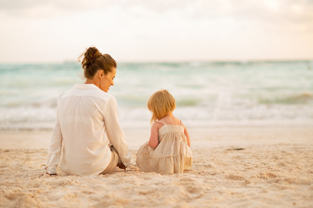 Mother and baby girl sitting on beach at the evening. rear viewの写真素材