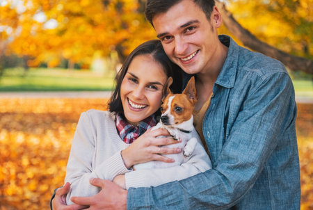 Portrait of happy young couple with dog outdoors in autumnの写真素材