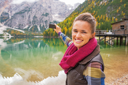 Happy young woman taking photo on lake braies in south tyrol, italy