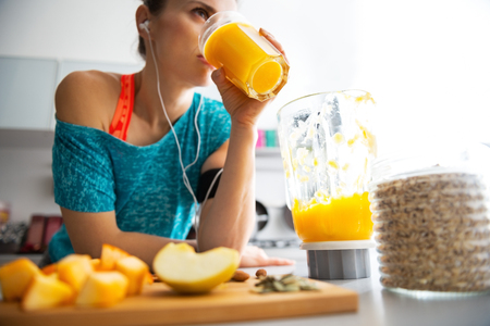 Close-up on fitness young woman drinking pumpkin smoothie in kitchen