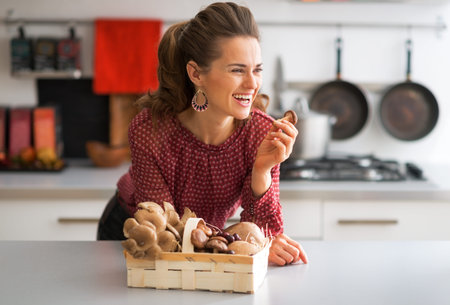 Portrait of happy young housewife with basket with mushrooms in kitchenの写真素材